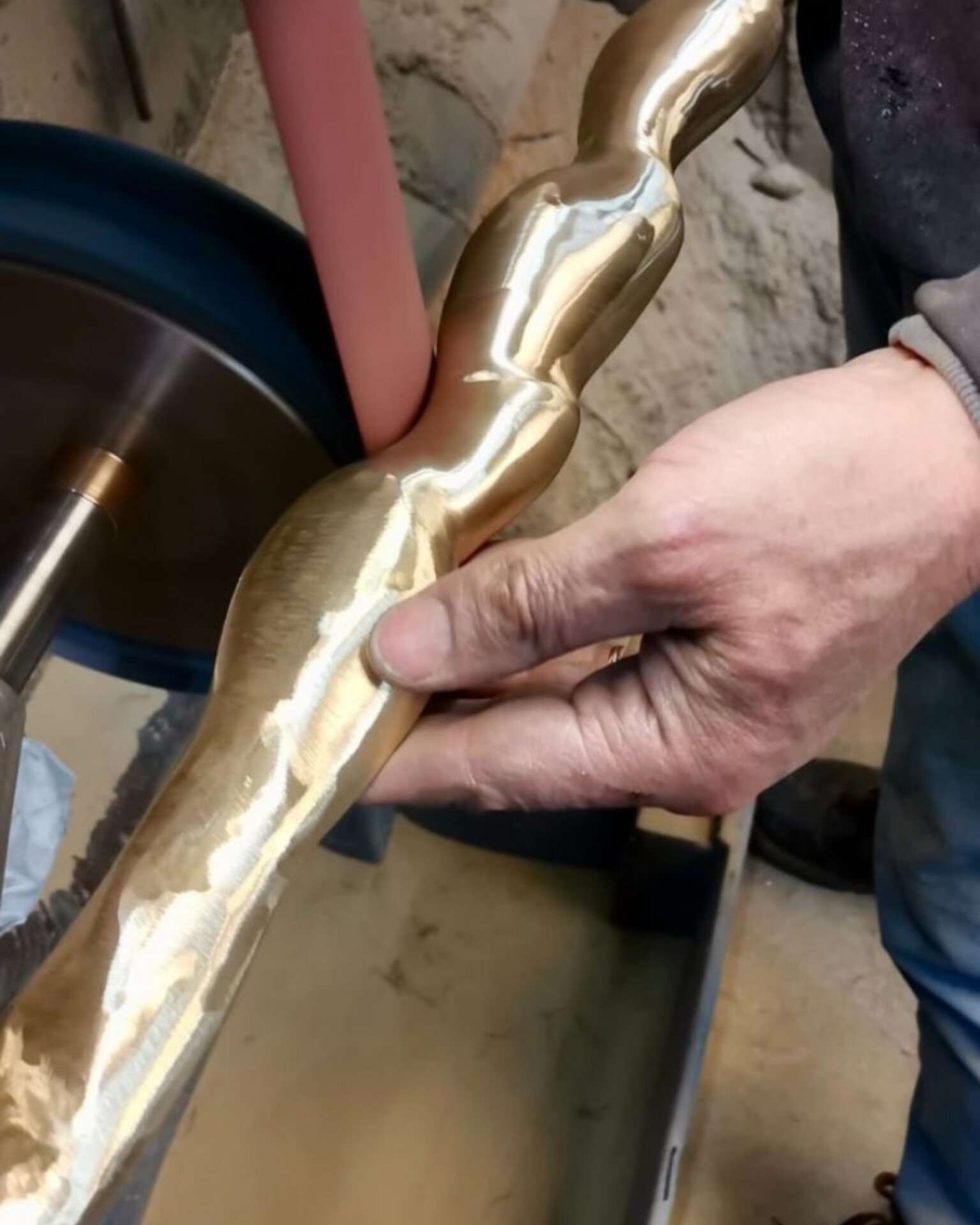 A craftsman's hands holding a custom-sculpted brass piece against a polishing belt, showing the transition from raw metal to high-shine finish.
