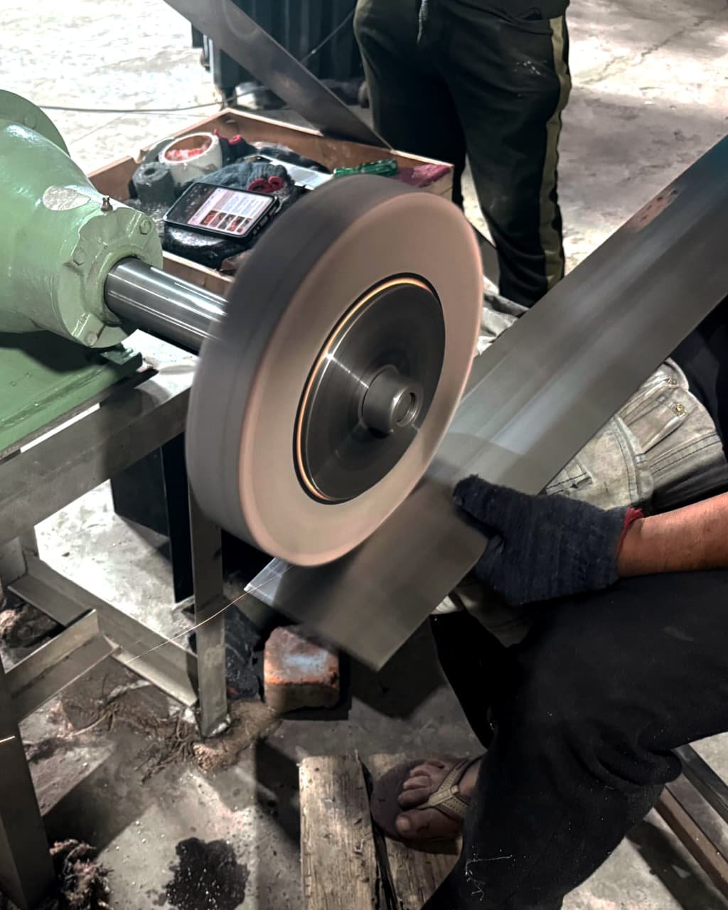 Craftsman polishing a steel furniture leg on a grinding wheel at Metal Shades metalwork studio, creating a hand-brushed finish