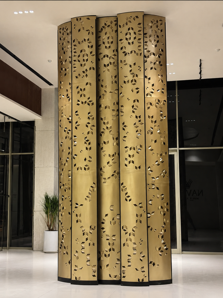 Gold finish perforated metal column cladding installed in a modern luxury lobby with decorative geometric cut patterns.