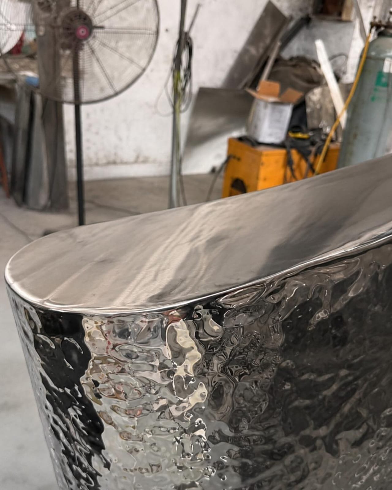 About Close-up shot of a modern luxury console table featuring a highly reflective, rippled hammered silver metal finish with a smooth, polished top surface.