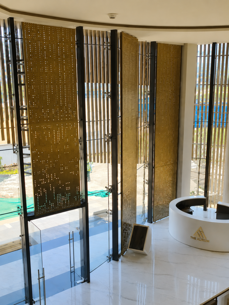 Luxury commercial lobby featuring bespoke brass perforated metal screens, glass entrance doors, and a custom reception desk by Metal Shades.