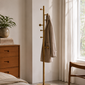 Modern brushed brass freestanding coat stand with multiple hooks in a minimalist bedroom interior.