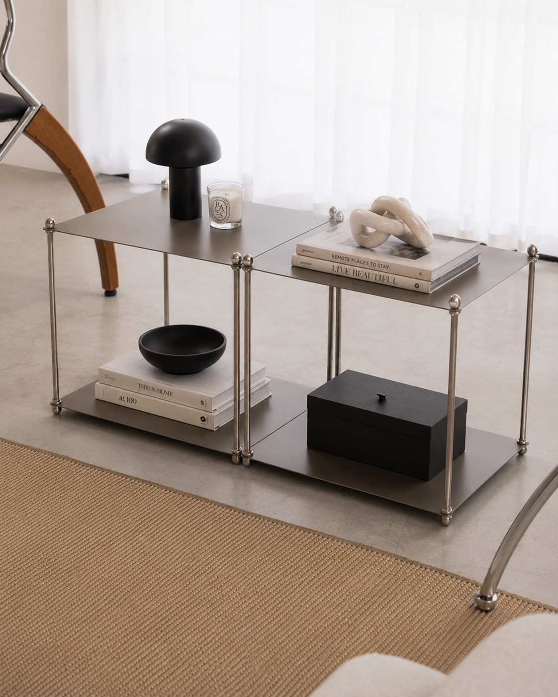Industrial-Style Modular Coffee Table with Mushroom Lamp and Decor Side angle of a gunmetal modular coffee table with silver rod legs, topped with a black mushroom lamp, candle, ceramic chain sculpture, and books, with a black bowl on the lower shelf
